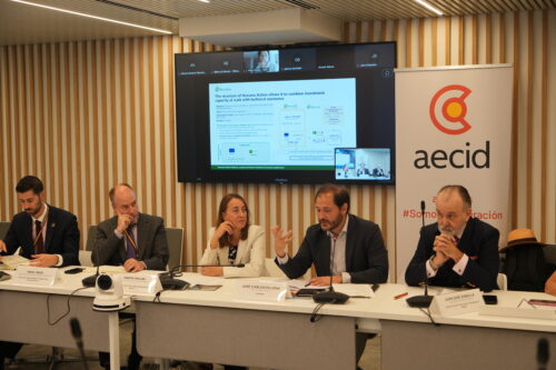 Mesa redonda sobre evaluación de Acción Huruma en la REPER, con cinco participantes y una presentación sobre Huruma Action proyectada en pantalla.